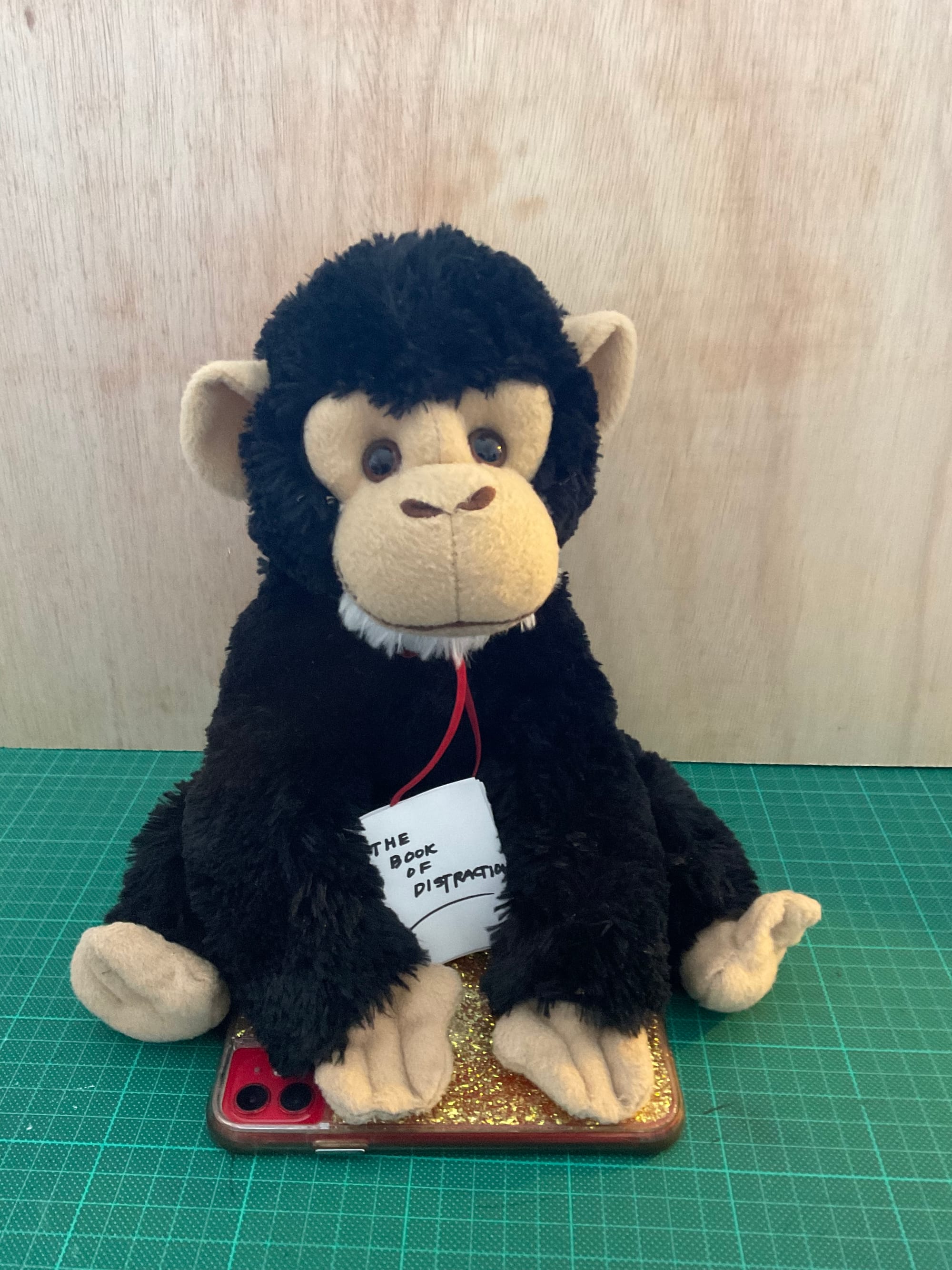 A stuffed howler monkey (of the toy variety not the real kind) sits with its paws resting on a smart phone. In its lap is a small book titled, "the book of distractions"